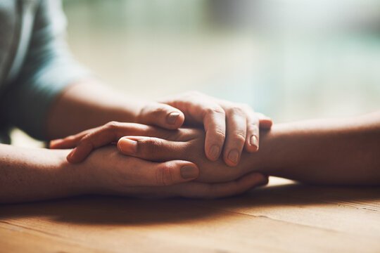 Love, empathy and support with people holding hands in comfort, care or understanding on a wooden table of a home
